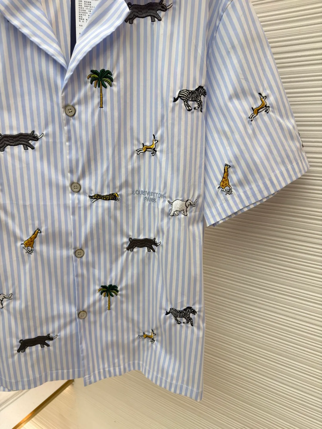 LOUIS VUITTON nostalgic style embroidered striped short-sleeved shirt with animals and plants ●Original version: Purchased and developed by 16815 ●Item number: 1682514-A65 ●Fabric: cotton fabric ●Technology: embroidery production ●Color: blue ●Version: fitted version ●Weight: about 220 grams ●Size: S-M-L-XL ●Description: This LOUIS VUITTON striped animal embroidery short-sleeved shirt is made of high-count pure cotton poplin fabric. After pre-washing process, it feels smooth and breathable. It has both drape and stiffness, and is not easy to wrinkle and deform. The blue and white vertical stripes on the body are woven with yarn-dyed technology, and the texture is clear and does not fade. The animal and coconut tree patterns are presented with sophisticated embroidery technology. The embroidery threads are full of color and the stitches are dense. The patterns are three-dimensional and vivid, forming a rich visual hierarchy with the stripe base. The shirt has a Cuban collar style, with smooth necklines, custom mother-of-pearl buttons at the placket, and a warm texture. The overall shape is loose, the shoulder joints are straight and fine, the cuffs are cuffed with exquisite craftsmanship, custom accessories and three logos are complete, and the details are full of luxury craftsmanship. It is suitable for casual vacations and daily outings, etc. The overall wiring is straight and delicate, the fabric is comfortable and soft, and the color is consistent without color difference. It can be matched with the same style to create a fashionable look and control various occasions. Customized accessories, complete with three standards, same style for men and women!
